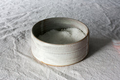 Wander Salt Pig: open-top white speckled ceramic dish filled with coarse salt, resting on wrinkled linen fabric.
