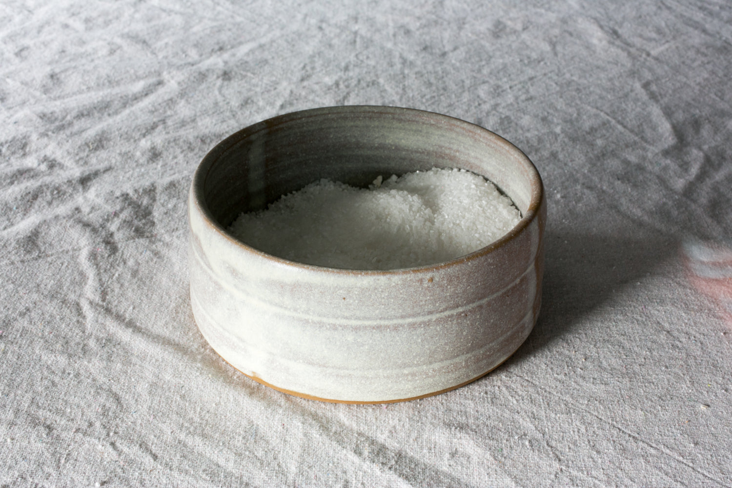 Wander Salt Pig: open-top white speckled ceramic dish filled with coarse salt, resting on wrinkled linen fabric.