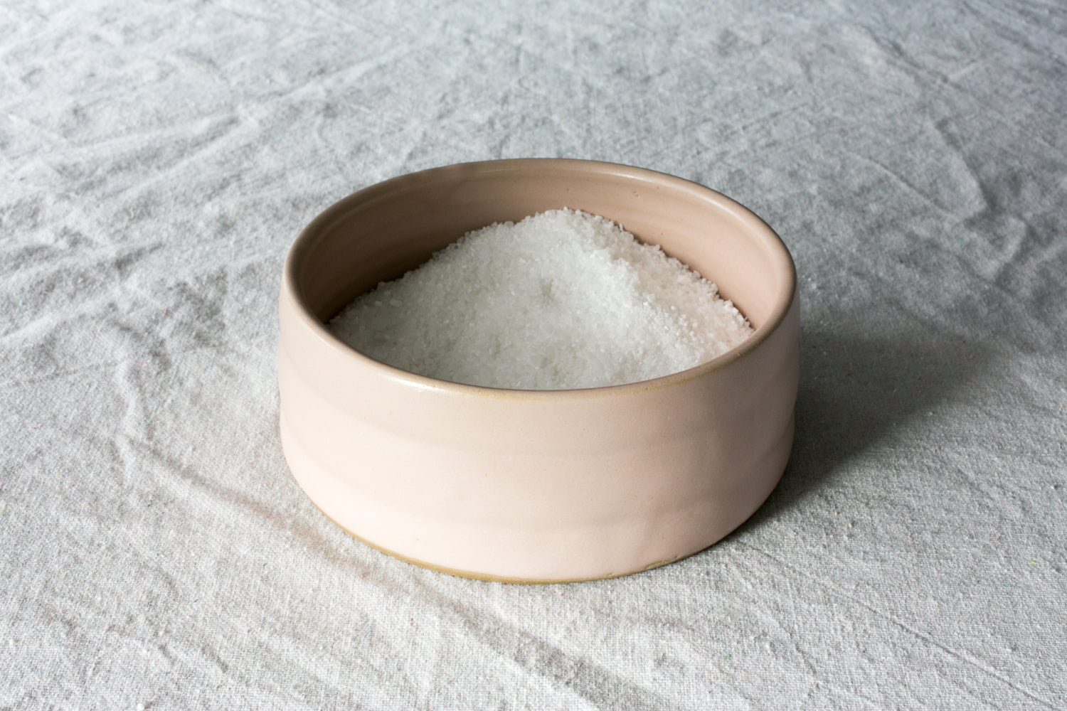 Wander Salt Pig: pale pink open-top ceramic salt cellar heaped with white sea salt on textured linen.