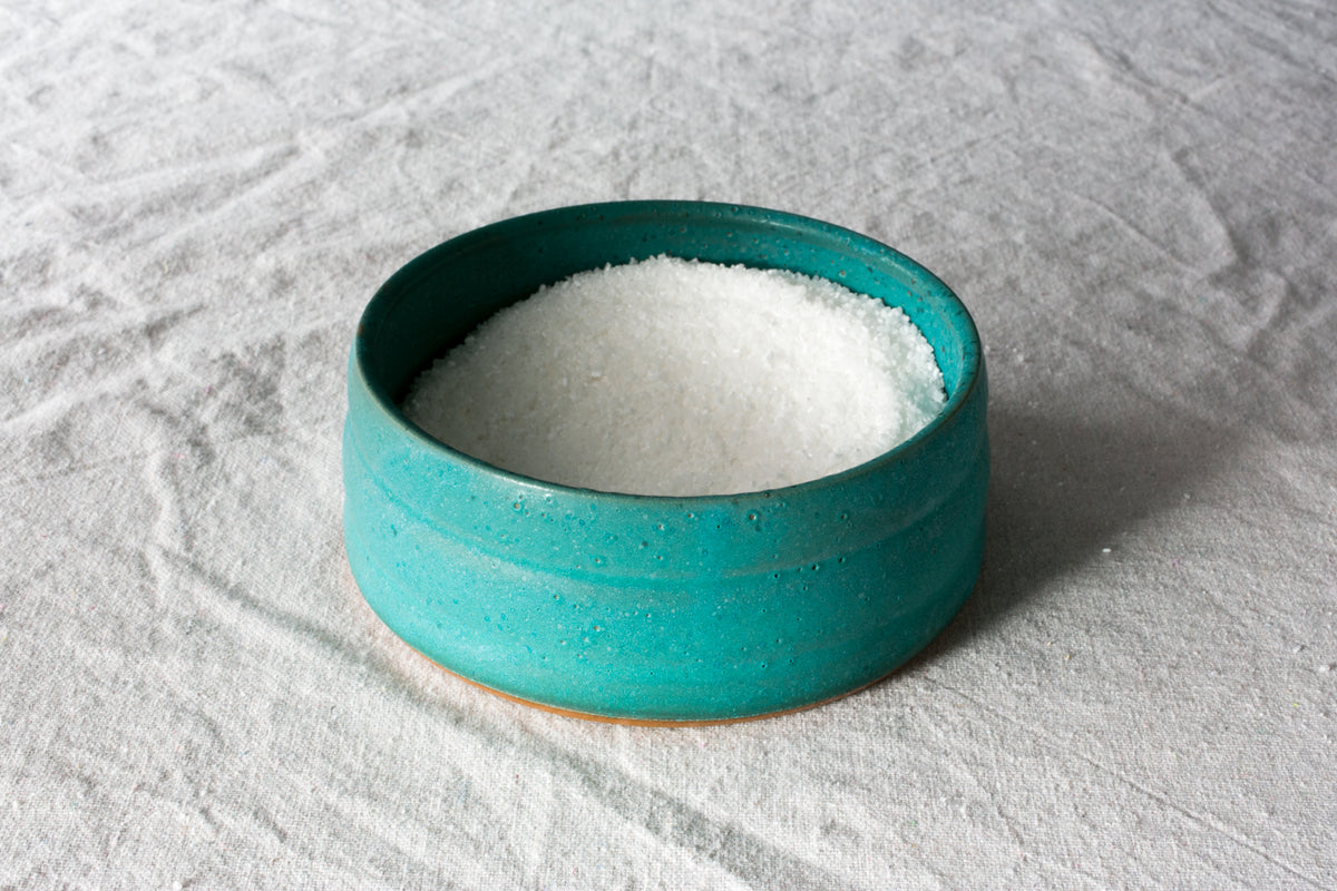 Wander Salt Pig: turquoise glazed open-top stoneware salt pig brimming with coarse salt on white cloth.