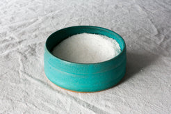 Wander Salt Pig: turquoise glazed open-top stoneware salt pig brimming with coarse salt on white cloth.