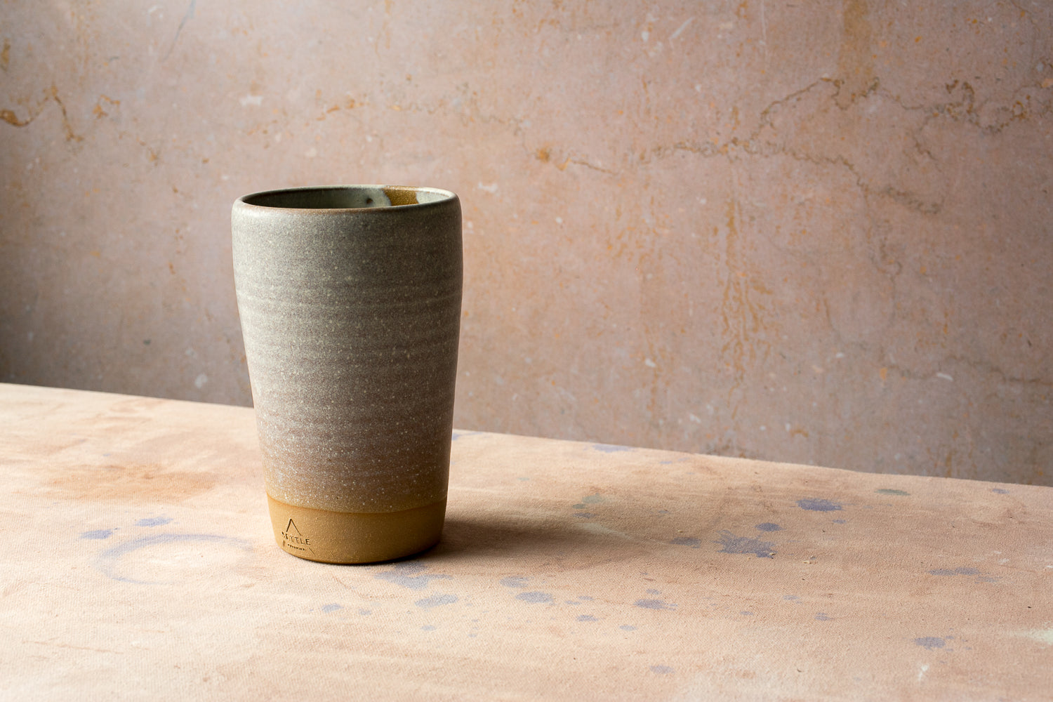 Wander Tall Tumbler in a speckled glaze with throwing rings and an impressed studio mark on the exposed clay foot.