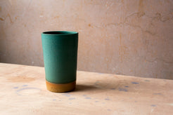 Wander Tall Tumbler in a dark teal glaze, displaying fine speckles and a crisp studio stamp on the raw clay base.