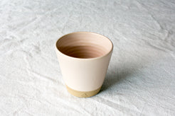 Wander Tumbler in smooth cream matte glaze, showing interior throwing rings and raw clay foot on linen fabric.