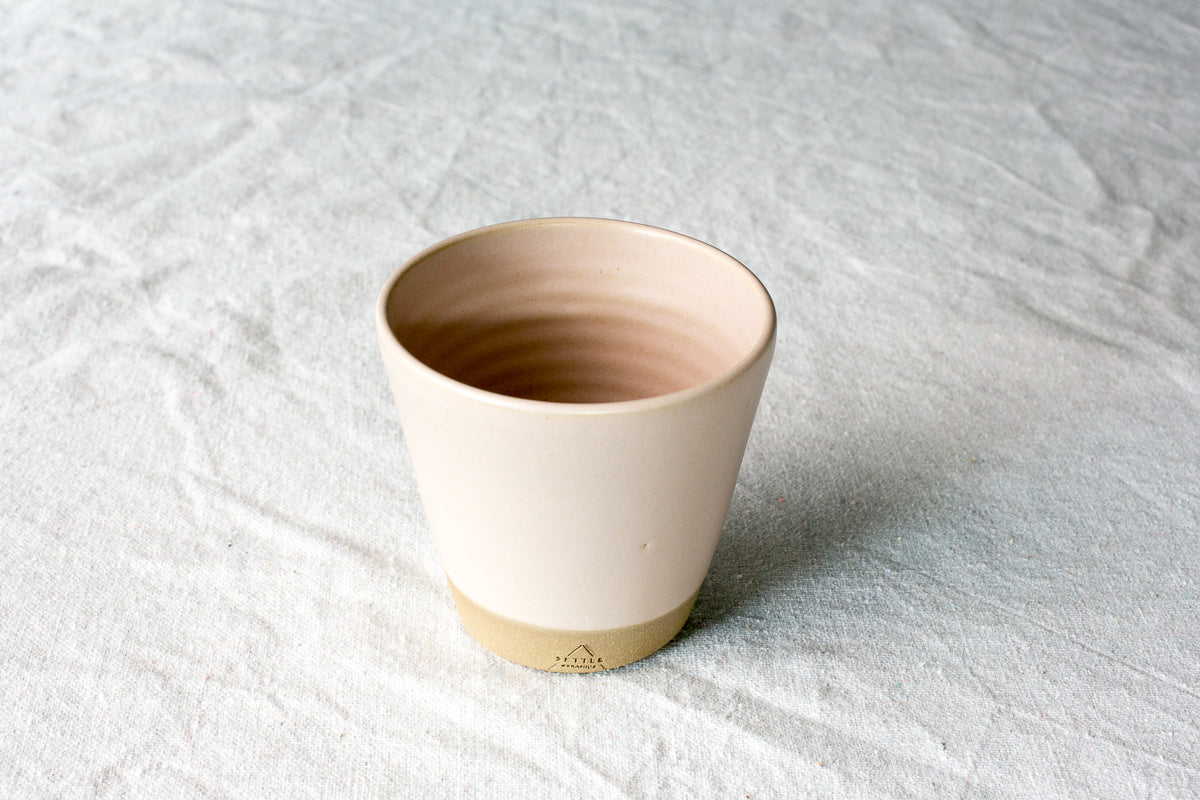 Wander Tumbler in smooth cream matte glaze, showing interior throwing rings and raw clay foot on linen fabric.